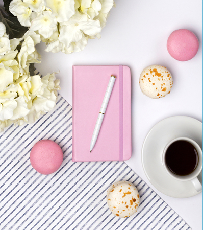 Pink notebook, pen, macaroons, coffee and flowers on white background. Female desktop, summer concept.の写真素材