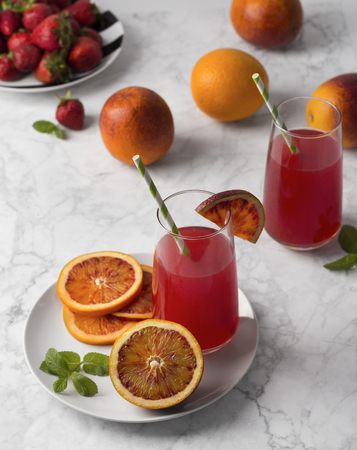Blood orange slices on the plate with mint leaf and knife. Whole and sliced fruits and glasses of juice on a light gray marble background.の写真素材