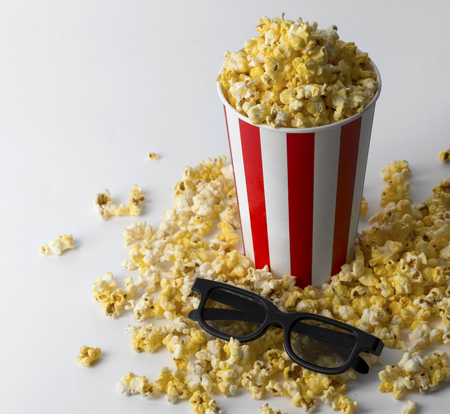 Popcorn in striped red bucket with 3d glasses at white background. Concept pastime, entertainment and cinema.の写真素材