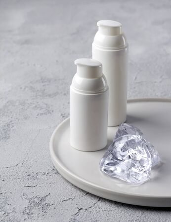 Two bottles of cosmetic cream with ice on gray concrete background. Blank label for branding mockup. Beauty and skin care conceptの写真素材