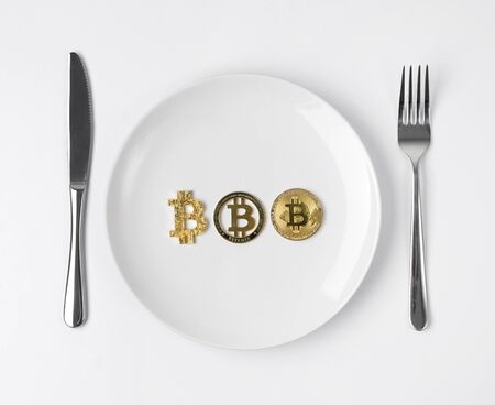 Three gold coins bitcoin served on white empty plateの写真素材