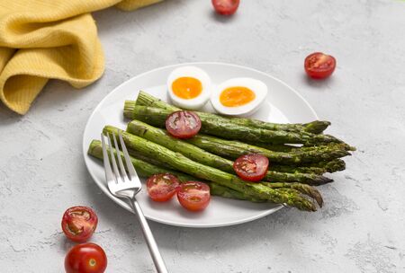Baked green asparagus, fresh tomatoes and boiled eggs with herbs on a plate on a concrete background. Restaurant menu recipe book  conceptの写真素材