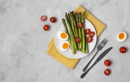 Baked green asparagus, fresh tomatoes and boiled eggs with herbs on a plate on a concrete background. Restaurant menu recipe book  conceptの写真素材