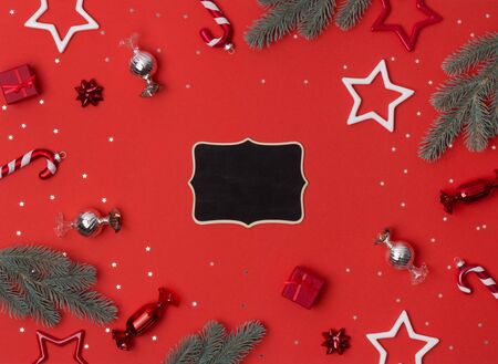 Christmas composition frame made of fir branches, bows, gifts, candy cane and star ornaments on red background. Flat lay, top view, copy spaceの写真素材