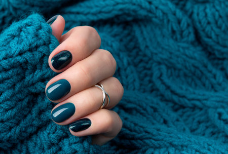 Manicured woman's hand in warm wool turquoise sweater. Fashionable autumn winter nail design.