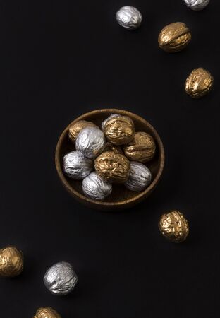 Painted golden and silver walnuts on wooden plate on black backgroundの写真素材