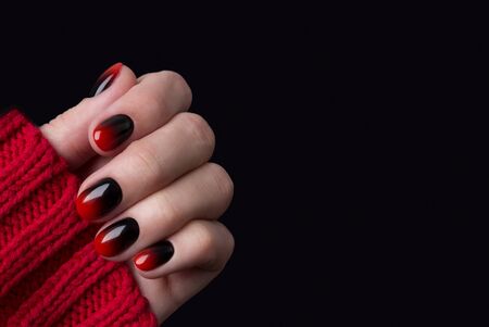 Female hand with red black ombre gradient nails in sweaterの写真素材