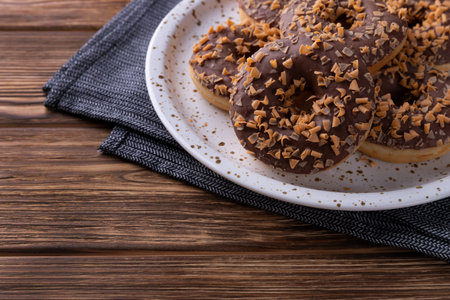 Glazed chocolate donuts on a plate on wooden background. Sweet food breakfast conceptの写真素材