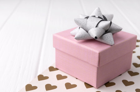 Pink gift box with silver bow on white wooden background with copy space. Minimal celebration...