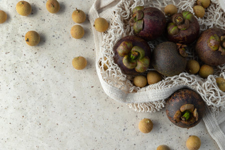 Flat lay composition with fresh ripe mangosteen and longan fruits in string bad on paper background