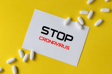 White pills and paper with  inscription on yellow background. Coronavirus treatment concept.の写真素材
