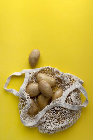 Flat lay top view raw organic potatoes in string bag on yellow backgroundの写真素材