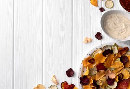 Crisp crunchy organic vegetable chips with oven-baked pumpkin, beetroot, tomato, carrot chips snacks with sauce on a white wooden table. Flat lay top view copy spaceの写真素材