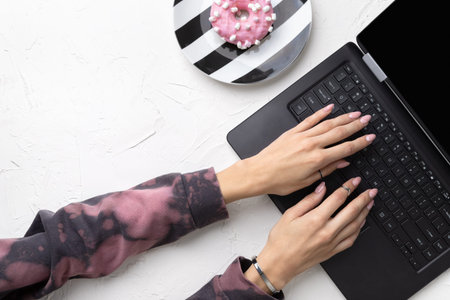 Manicured woman's hands in trendy pink hoodie typing on laptop. Fashionable spring summer nail design. Work business office templateの写真素材