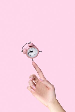 Alarm clock balancing on womans hand on pink backgroundの写真素材
