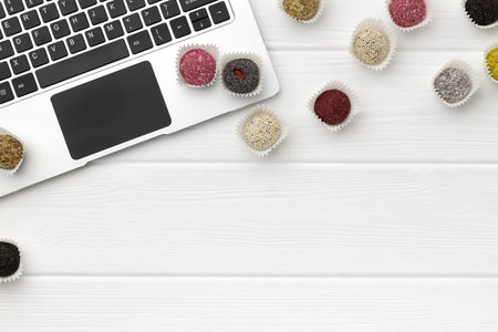 Vegan sweets energy balls near the laptop on white wooden table. Online food delivery concept