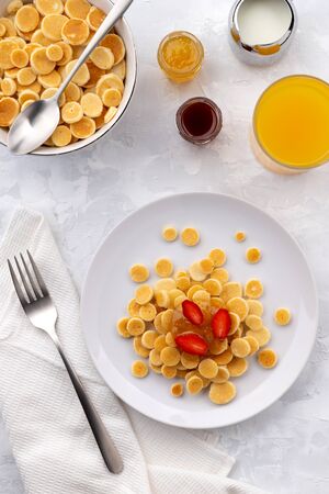 Tiny mini pancake cereal. Home made breakfast with raspberries, jam and juice on gray background. Trendy morning food flat lay top viewの写真素材