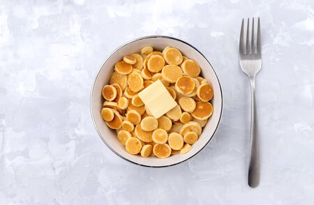 Tiny mini pancake cereal. Homemade breakfast with butter on gray background. Trendy morning food flat lay top viewの写真素材