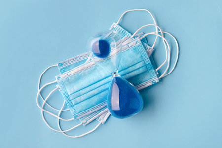 Hourglass with medical mask on a blue background. End of quarantine concept