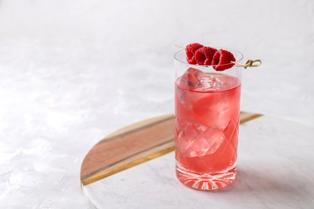 Pink rose iced cocktail with raspberry in crystal glass on table. Summer refreshment drinks.