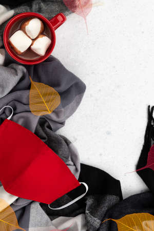 Red cup with hot cocoa, scarf and face mask on gray background. Flat lay top view new normal autumn winter composition.の写真素材