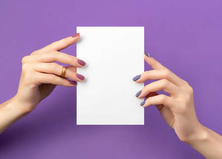 Beautiful womans hand with manicure holding postcard on purple background. Beauty salon business card template.の写真素材