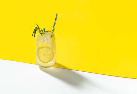Glass ice lemonade with rosemary on yellow background. Minimal style composition summer drink restaurant template.の写真素材