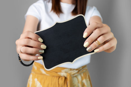 Woman's hands with yellow shiny nail design holding wooden sign. Fashionable trendy female manicure...