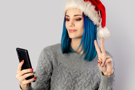Beautiful happy young woman in santa hat take selfie over gray background. Christmas new year...
