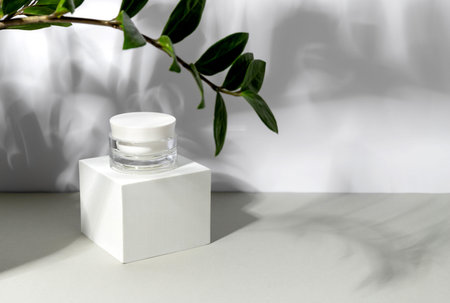 Bottle of cosmetic cream on gray background in sunlight with shadows of leaves. Minimal style...