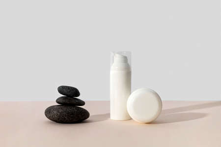 Bottles of cosmetic cream with balancing stones on beige background in sunlight. Minimal style cosmetics templateの写真素材