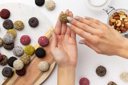 Colorful vegan candies energy balls on a plate with womans hand isolated white backgroundの写真素材