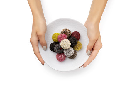 Colorful vegan candies energy balls on a plate with womans hands isolated white background