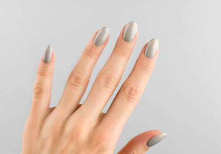 Beautiful womans hand with manicure close up on gray background. Gray nail polish. Beauty salon concept.の写真素材