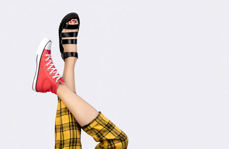 Legs of a young woman in trendy red sneakers and sandals on gray background. Footwear shopping sale conceptの写真素材