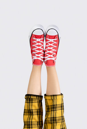 Legs of a young woman in stylish red sneakers on gray background.