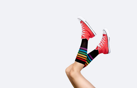 Womens legs in stylish red sneakers and rainbow socks on gray background