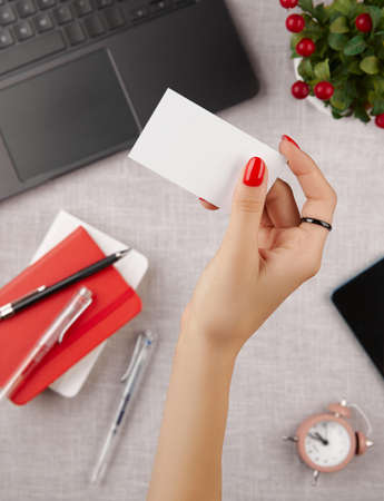 Woman with red manicure holding blank business card on gray tableの写真素材