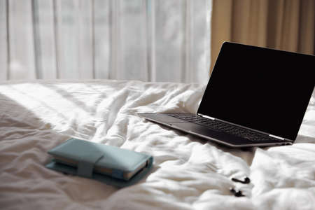 Laptop, planner and headphones on bed in sunlightの写真素材