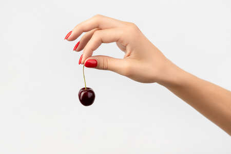 Womans hand with red manicure holding cherryの写真素材