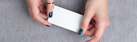 Manicured womans hands holding business card on grey furry background
