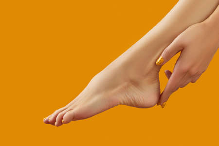 Female leg and hand with summer nail design on orange backgroundの写真素材