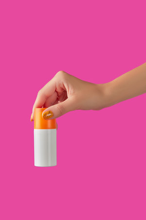 Manicured womans hand holding sunscreen bottle on pink background