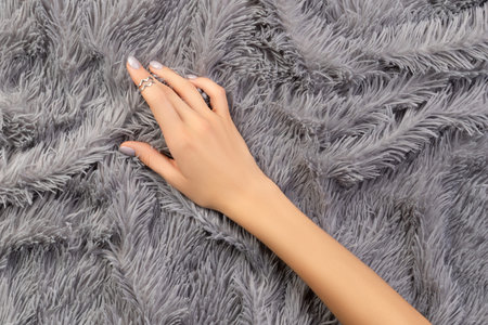 Womans hand holding on furry gray cover.