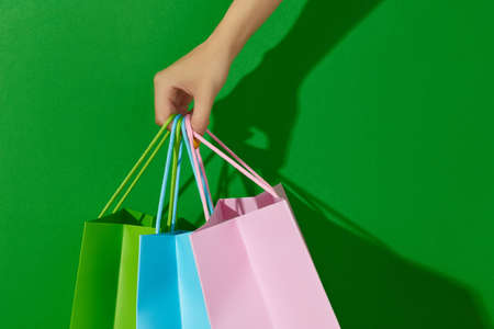 Womans hand holding shopping bags on green background. Shopping sale conceptの写真素材