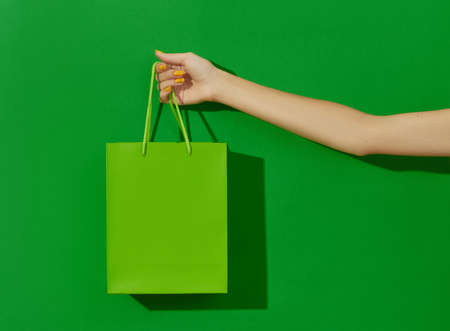 Womans hand holding shopping bag on green background. Shopping sale conceptの写真素材