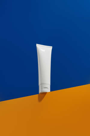 Blank white tube bottle with skin care product on blue and orange creative backgroundの写真素材