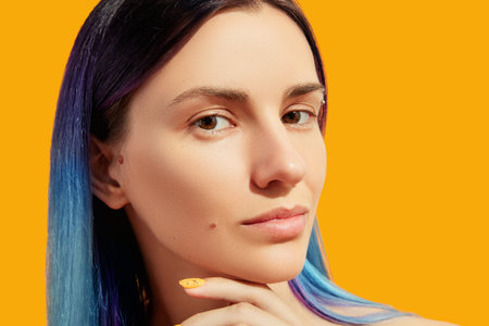 Face of young beautiful woman with blue hair on yellow background.