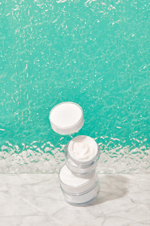Balancing jars with cosmetic cream on turquoise background