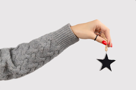 Hand with manicure holding star ornaments on gray background with copy space